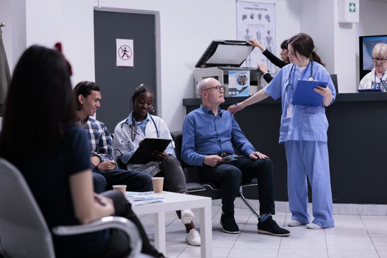 Caring nurse taking senior patient to see medic for clinical consult while african american doctor is completing form for asian patient. Diverse people waiting in modern hospital reception.