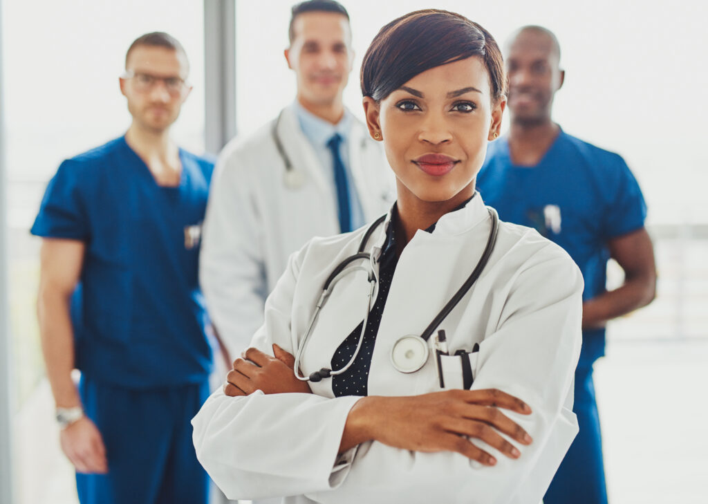 Black female doctor in front of team, looking at camera with preventative healthcare medical team in background.