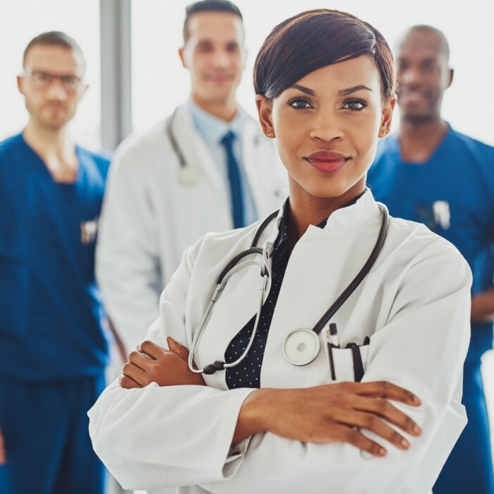 Black female doctor in front of team, looking at camera with preventative healthcare medical team in background.