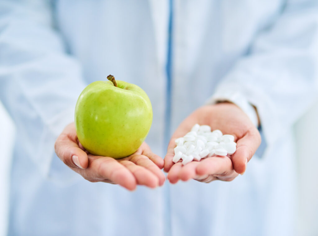 Closeup shot of an doctor holding an apple and a variety of pills in her hands as contrast between conventional and functional medicine.