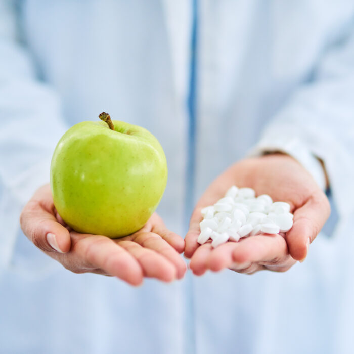 Closeup shot of an doctor holding an apple and a variety of pills in her hands as contrast between conventional and functional medicine.