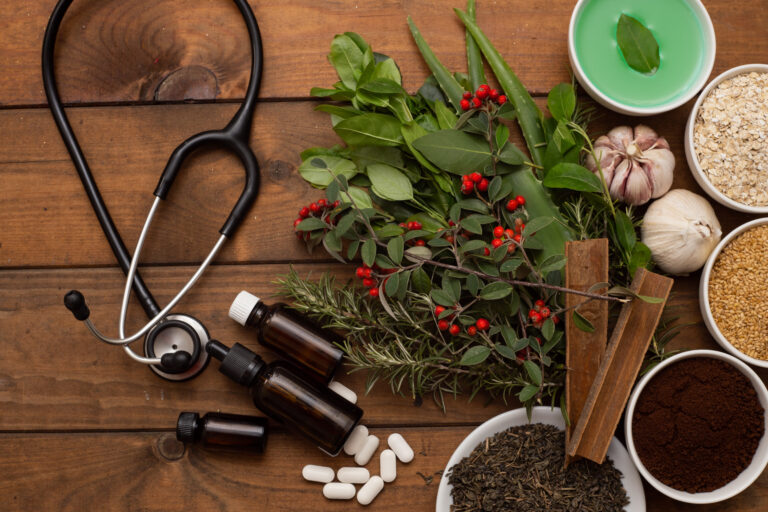 A top view of a stethoscope next to herbs, spices, pills and other functional medicine items.