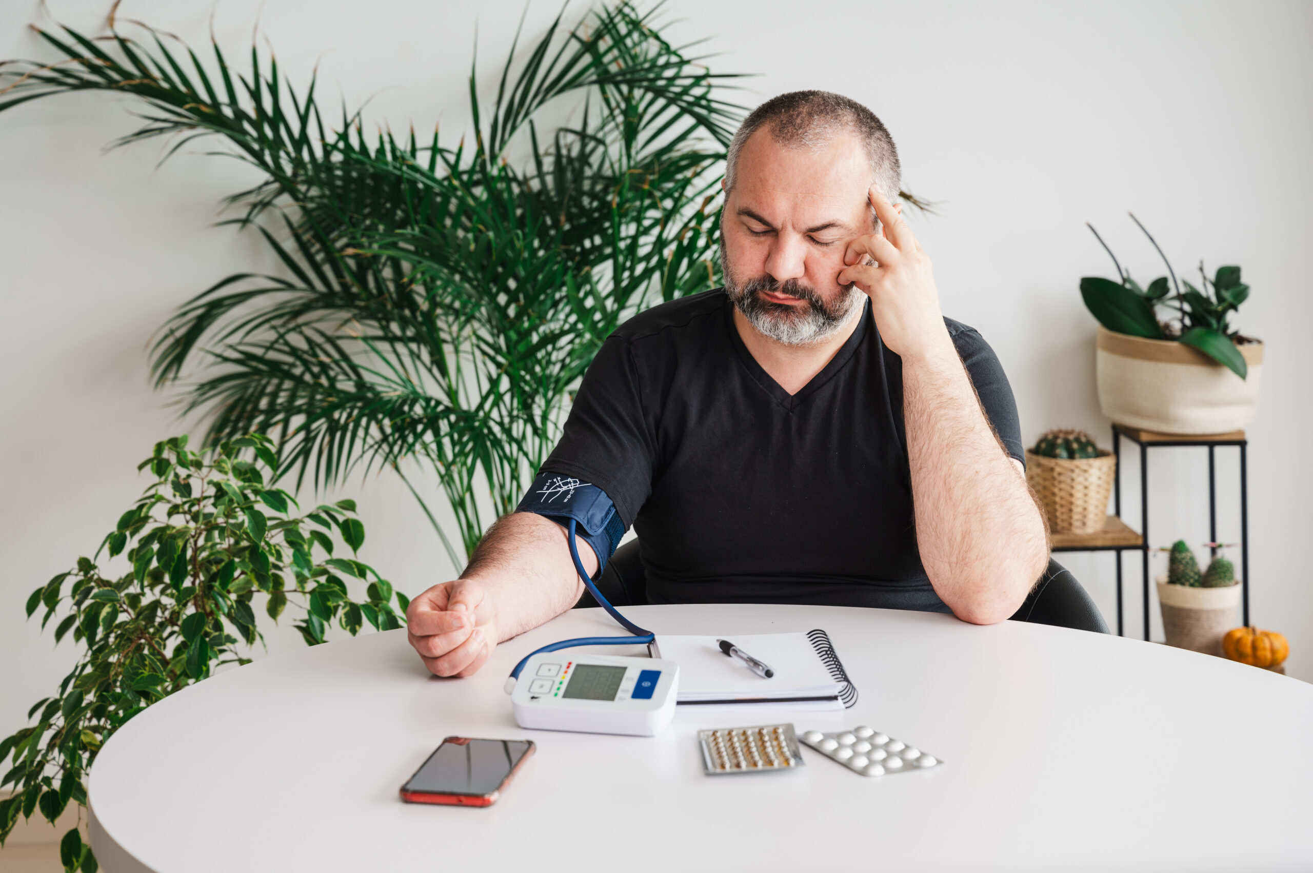 Man checking his blood pressure while experiencing symptoms that may be associated with low testosterone and hormone imbalance.