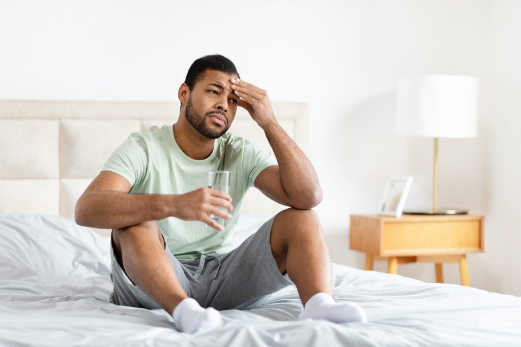Man feeling fatigued while sitting on the edge of his bed, illustrating reduced energy associated with low testosterone.