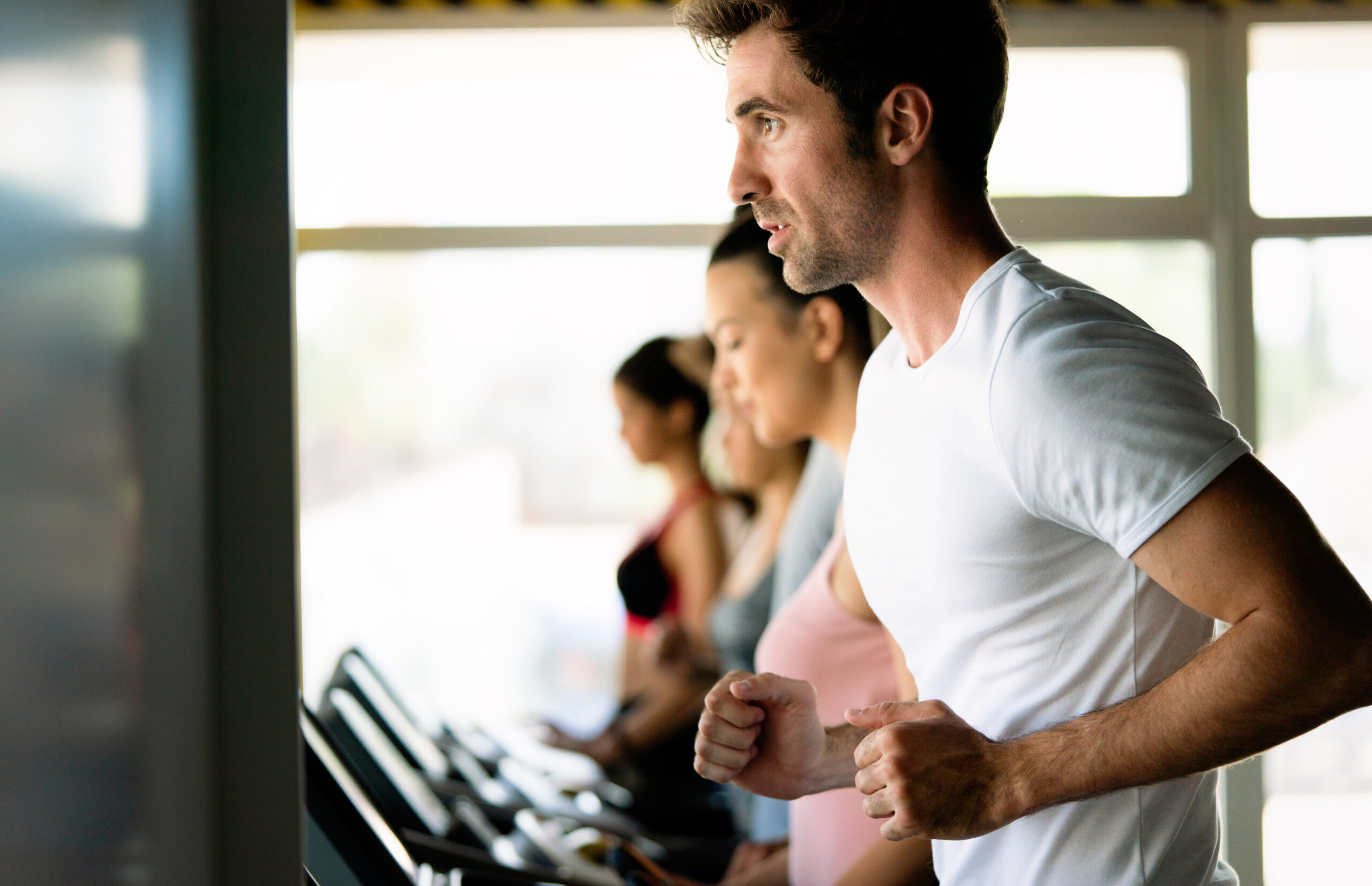 Group of young fit people running on treadmills in modern sport gym.