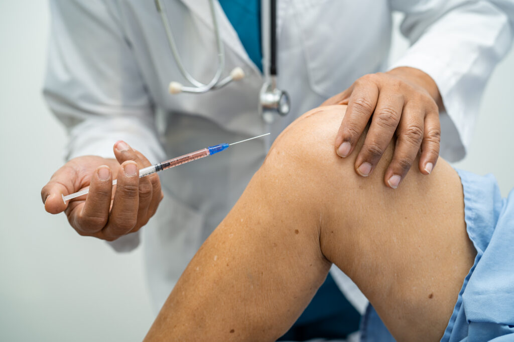 Close-up of a healthcare professional positioning a syringe near a patient’s knee for joint pain treatment.