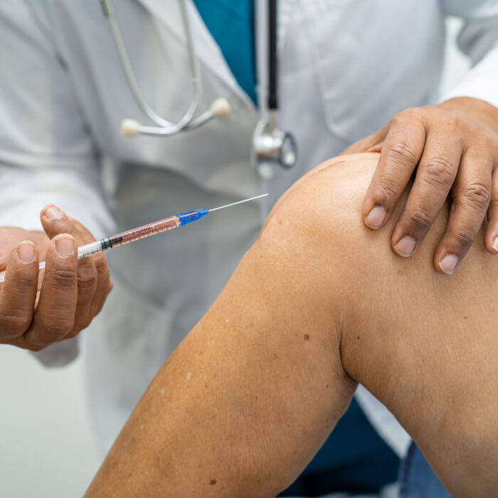 Close-up of a healthcare professional positioning a syringe near a patient’s knee for joint pain treatment.