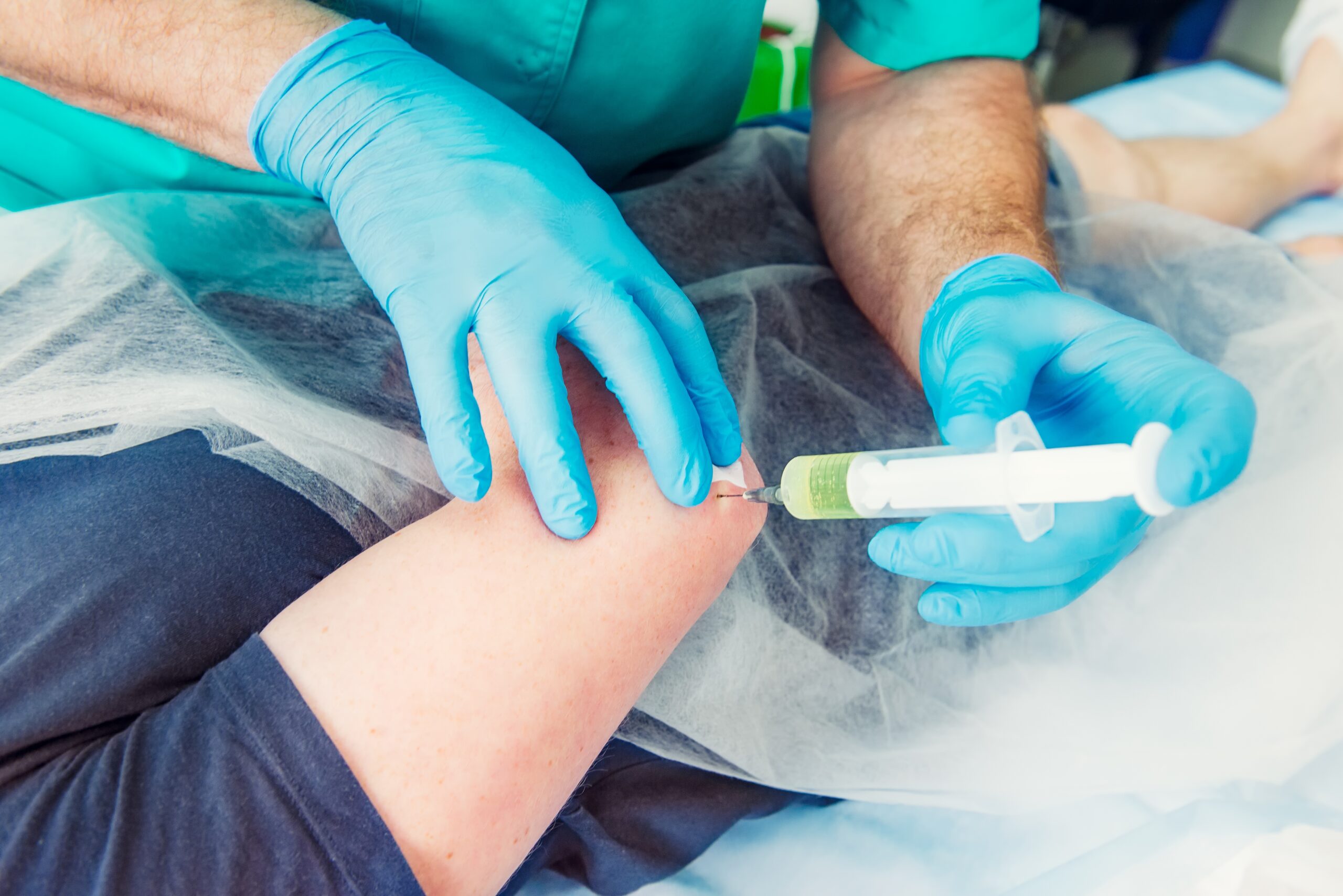 Healthcare professional administering an injection near a patient’s knee as part of musculoskeletal treatment.