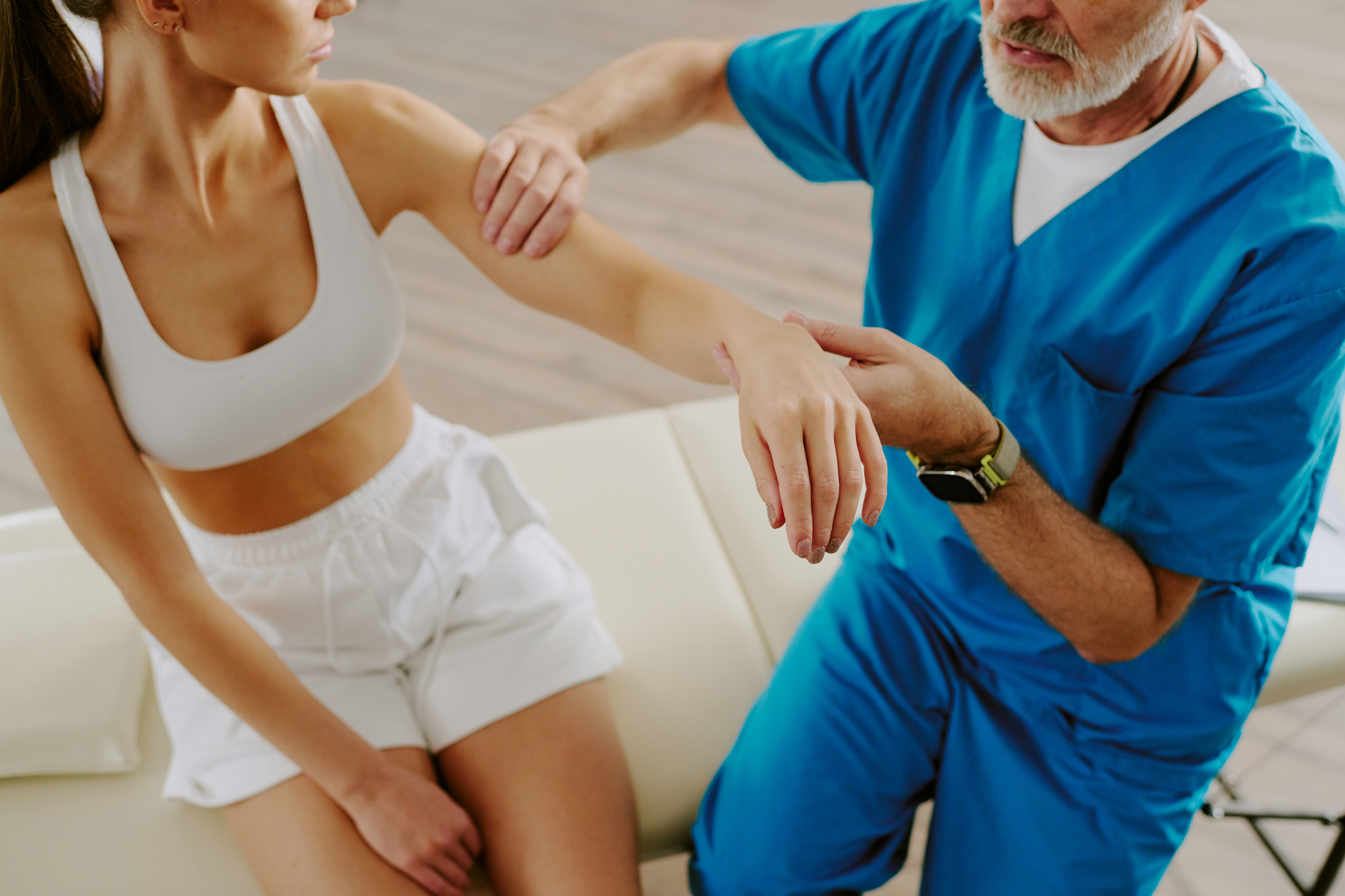 Healthcare professional assessing a woman’s arm during a consultation for musculoskeletal pain.